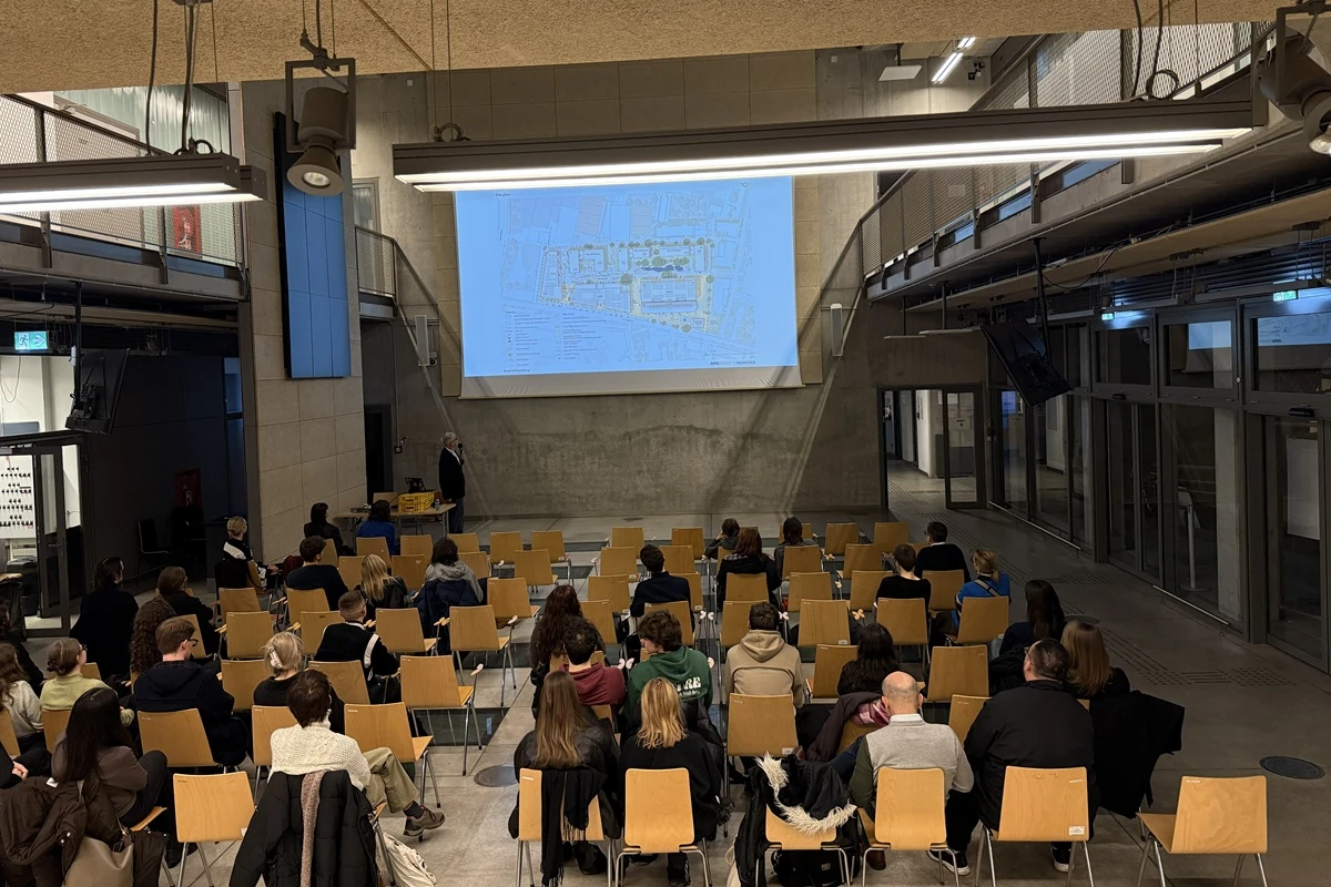 Uczestnicy wykładu Szymona Wojciechowskiego na tle prezentacji projektów APA